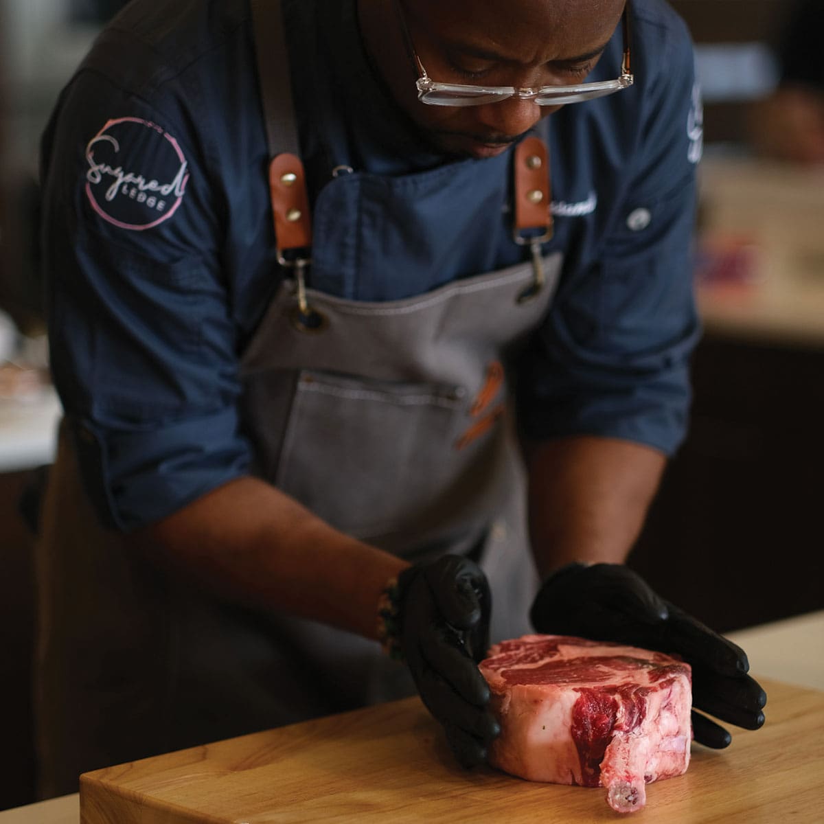 a chef with an apron is holding an uncooked steak.